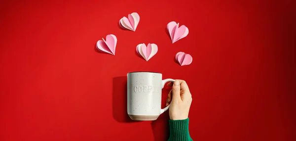 Female hand holding a mug with paper craft hearts — Stock Photo, Image
