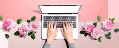 Laptopunu pembe güllerle kullanan bir kadın.