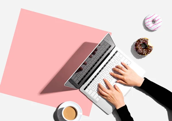 Osoba korzystająca z laptopa z pączkiem i filiżanką kawy — Zdjęcie stockowe