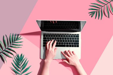 Tropikal yaprakları olan bir dizüstü bilgisayar kullanan kişi