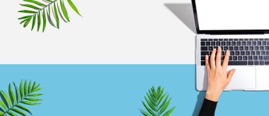 Yukarıdan gelen tropikal yapraklı bir dizüstü bilgisayar kullanan kişi