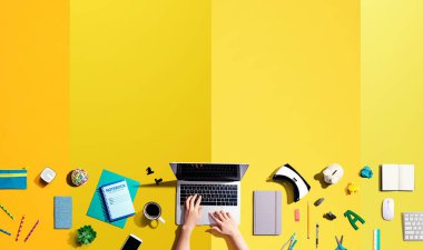 Ofis malzemelerinin olduğu bir dizüstü bilgisayar kullanan kişi.