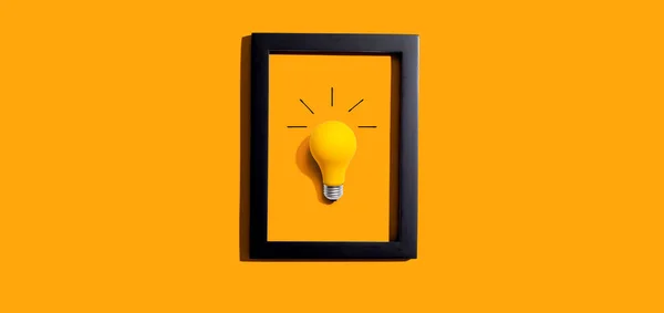 Yellow light bulb inside a frame - inspiration, creativity, energy, electricity themes