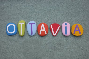 Ottavia, female given name composed with hand painted multi colored stone letters over green sand