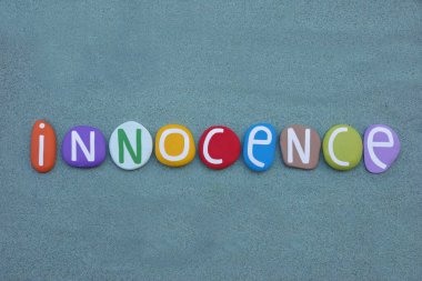 Masumiyet, yeşil kum üzerinde çok renkli taş harflerle oluşturulmuş yaratıcı kelime.