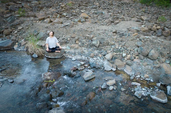 若い女性は川沿いの屋外で瞑想。ヨガは自然の中で運動します。ドローン航空写真 — ストック写真
