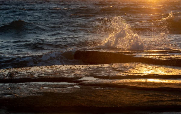Stormiga blåsiga havsvågor plaskar på en stenig kust vid solnedgången — Stockfoto