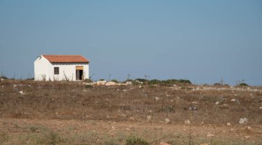 Terk edilmiş beyaz ev mavi gökyüzüne karşı tarlada.