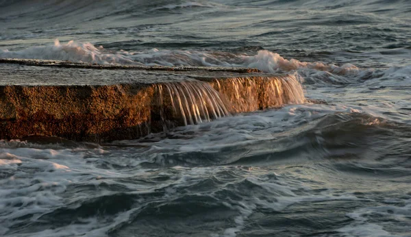 Fırtınalı rüzgarlı deniz dalgaları gün batımında kayalık bir sahile vuruyor. — Stok fotoğraf