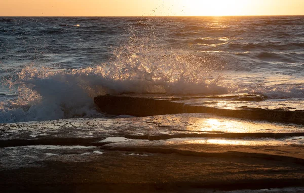 Stormachtige winderige zee golven spatten op een rotsachtige kust bij zonsondergang — Stockfoto
