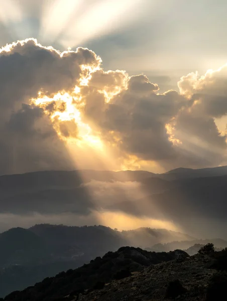 해질 녘에 산 위의 먹구름 사이로 밝은 태양 광선 이비치고 있다. 뜨거운 겨울 하늘 — 스톡 사진