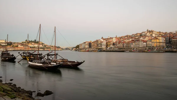 Tradycyjne łodzie załadowane beczkami wina zacumowane w rzece Douro naprzeciwko starego miasta nad brzegiem rzeki rano. — Zdjęcie stockowe