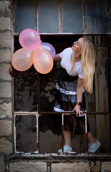 Mujer feliz divirtiéndose sosteniendo globos de aire de colores en una ventana rota —  Fotos de Stock