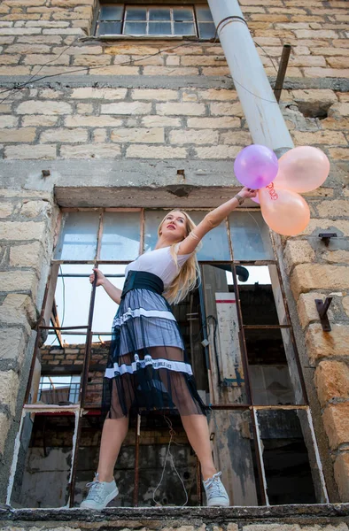 Mulher feliz se divertindo segurando balões de ar coloridos em uma janela quebrada — Fotografia de Stock