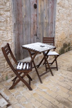 Boş kar kaplı ahşap sandalyeler ve taşlaşmış bir patikada kahve masası..