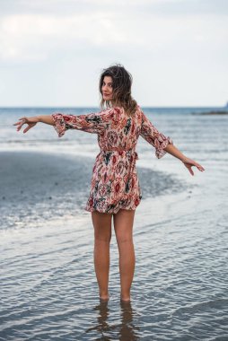 Kumsalda elini kolunu açmış özgürce yürüyen bir kadın. Okyanusun tadını çıkarıyorum Yaz tatili