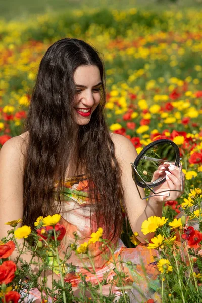 Mladá dívka s dlouhými vlasy se na jaře dívá do zrcadla na poli. Atraktivní mladá žena na jaře — Stock fotografie