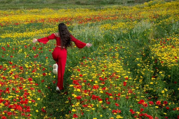 Šťastná žena v červených šatech běží na poli na jaře — Stock fotografie