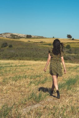 Genç ve çekici bir kadın baharda tarlada yürüyor. Moda tarzı açık hava.