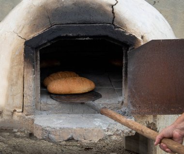 Geleneksel kil fırında pişirilmiş taze ev yapımı ekmek. Elinde sopayla ekmek tutan kişi