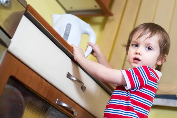 Pequeño bebé está alcanzando hervidor eléctrico con agua caliente —  Fotos de Stock