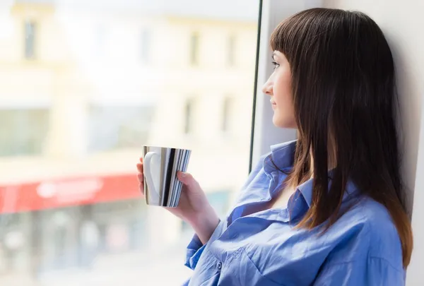 Γυναίκα με ένα φλιτζάνι τσάι, ψάχνει μέσα από το παράθυρο — Φωτογραφία Αρχείου