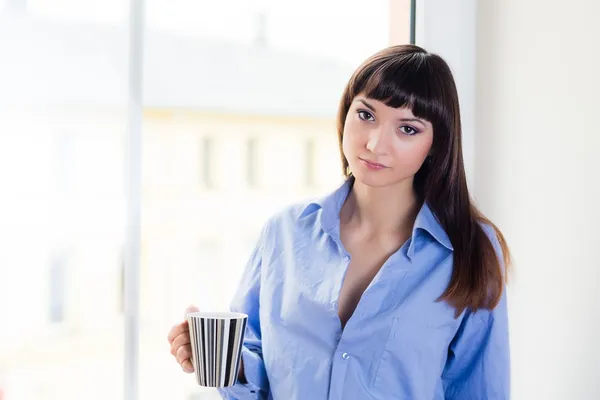 Brunette in a blue shirt holding a cup — Stock Photo, Image