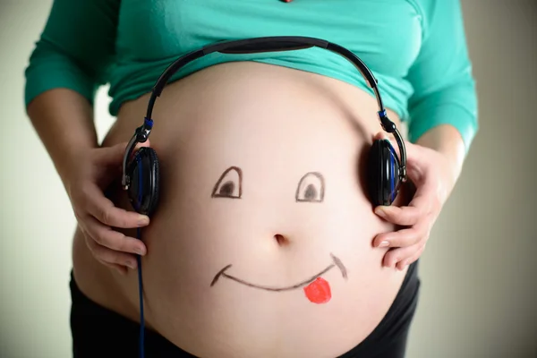 Pregnant belly listens to music through headphones — Stock Photo, Image