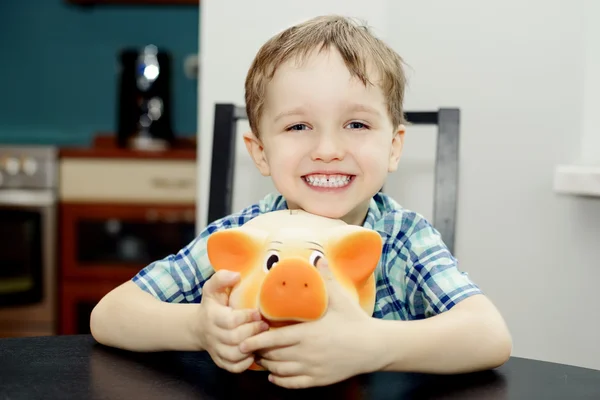 4 year old boy smiling while holding a piggy bank — Stock Photo, Image