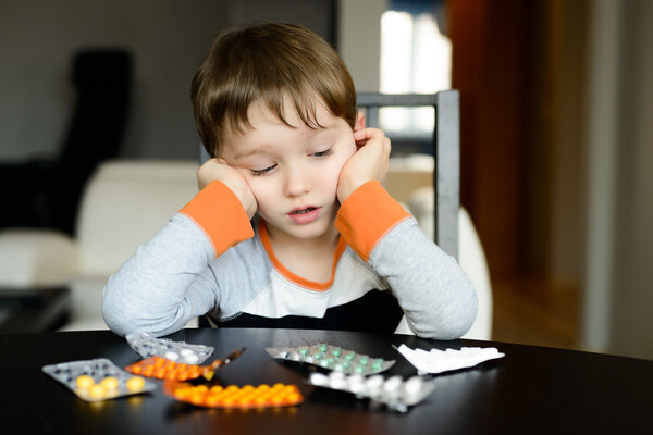 worried 4 year old boy sitting at the table with medications
