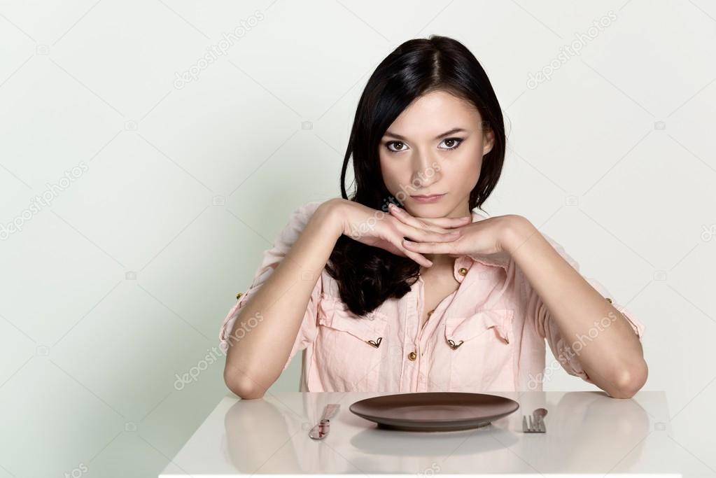 Beautiful brunette woman sitting with an empty plate and wait her lunch