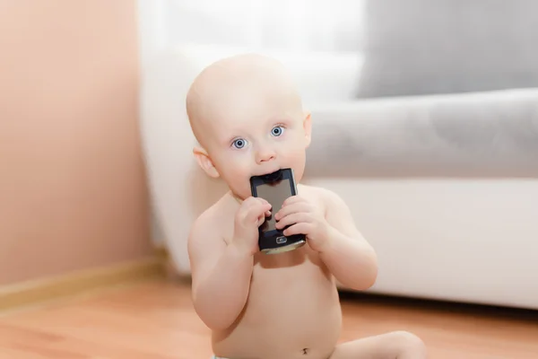 Ahşap yerde oturan ve bir cep telefonu ile oynayan bebek — Stok fotoğraf