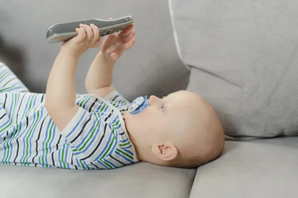 Baby lying on a sofa and playing with TV remote control — Stock Photo, Image