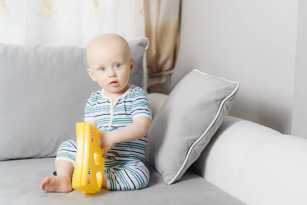 Pequeño bebé sentado en el sofá y jugando con el juguete — Foto de Stock