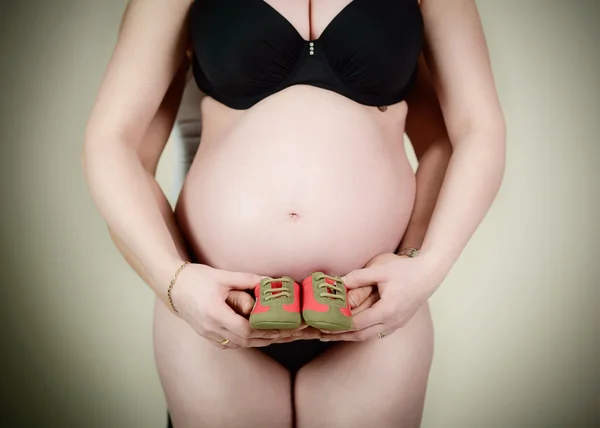 Papai e mamãe estão segurando pequenos sapatos de bebê perto da gravidez mulheres barriga — Fotografia de Stock