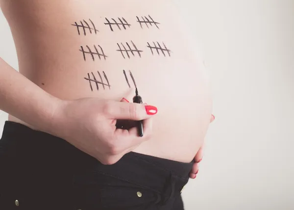 Pregnant woman painting bars on her belly — Stock Photo, Image