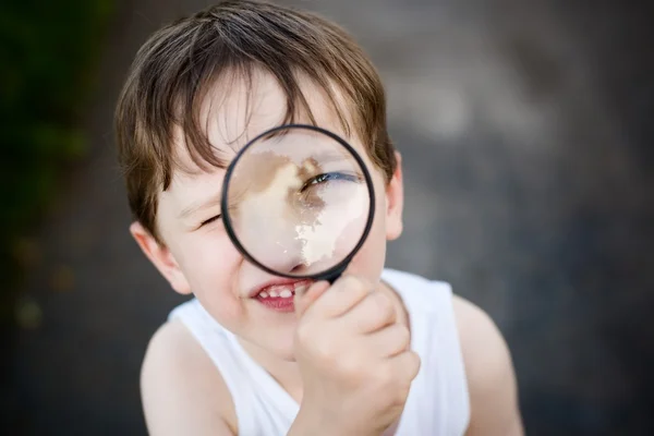 Little boy puts a magnifying glass to eye — Stock Photo, Image