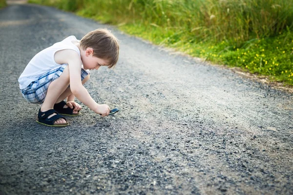Bambino che guarda le pietre sdraiato su una strada sterrata attraverso una lente d'ingrandimento — Foto Stock