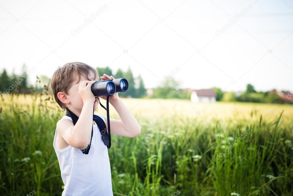  little boy in a field looking through binoculars