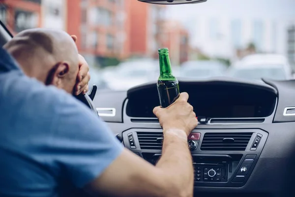 El hombre conduce un coche con una botella de cerveza al volante de un coche. — Foto de Stock