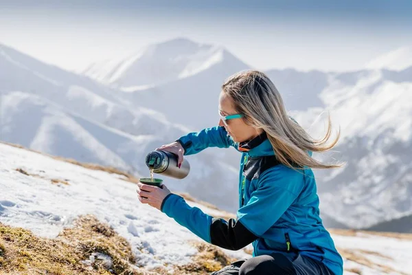 Жінка наливає і п'є гарячий чай або каву з термоса на зимовий гірський слід — стокове фото