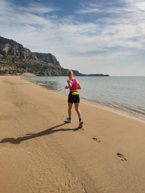 Spor giyimli güzel sarışın kadın Yunanistan 'ın Rodos, Yunanistan' daki Tsampika plajında büyük bir kayanın yanında dinleniyor.