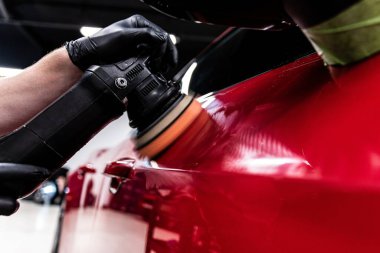 Araba yıkama ya da araba yıkama atölyesi çalışanı araba boyasını elektrikli cilasıyla parlatır.