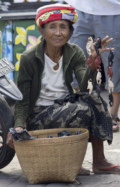 BALI, INDONESIA-JUNE 24TH: An old woman selling monkey trinkets — Stock Photo, Image