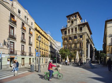 Madrid, İspanya - 8 Kasım 2021. Güneşli bir günde Plaza de Ramales Meydanı 'ndan geçen bir bisikletçi. Arka planda Ricardo Augustin Sarayı var. Madrid, İspanya.