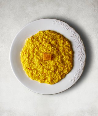 Safran ipliklerle kaplı Risotto alla Milano ve beyaz taş bir masanın üzerinde Parmigiano peyniri kabuğu. İtalyan mutfağı.