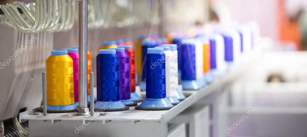 Colorful rows spools of thread stand on embroidery machine in garment industry.