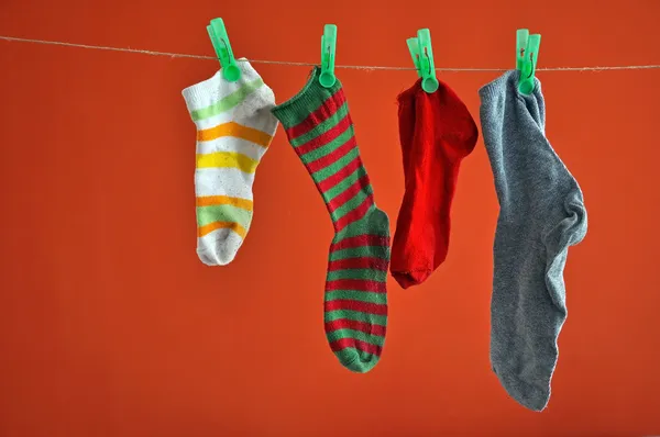Diferentes tipos de calcetines a rayas que cuelgan de una cuerda aislada en rojo Imagen de archivo