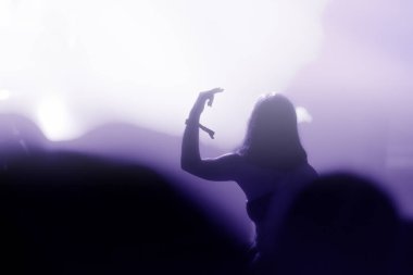 Konserde kollarını açarak kalabalığın dikey görüntüsü. Arka planda parlak sahne ışıkları