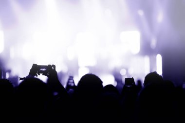 Ellerin silueti akıllı telefonlarla bir konser kaydediyor. Konseri fotoğraflamak için akıllı telefon kullanan bir sürü insan var.